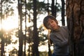 Funny little girl peeking out from behind tree in winter park. Cute smiling child playing hide and seek in the forest. Children Royalty Free Stock Photo