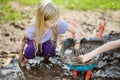 Funny little girl playing in a large wet mud puddle on sunny summer day. Child getting dirty while digging in muddy soil. Royalty Free Stock Photo