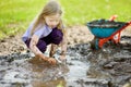 Funny little girl playing in a large wet mud puddle on sunny summer day. Child getting dirty while digging in muddy soil. Royalty Free Stock Photo