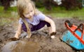 Funny little girl playing in a large wet mud puddle on sunny summer day. Child getting dirty while digging in muddy soil Royalty Free Stock Photo