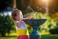 A funny little girl is playing with the spray of a drinking water fountain in the park. Childhood, child, summer time, heat. Solar Royalty Free Stock Photo