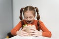 Funny little girl with ponytails biting a sandwich with a grin on her face. Cute hungry kid eating a pita souvlaki snack in a Royalty Free Stock Photo