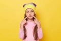 Funny little girl with ponytails wearing pink shirt and beanie hat standing isolated over yellow background pointing at her pout Royalty Free Stock Photo