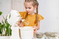 The funny little girl prepares dough or cream in a submersible mixer.