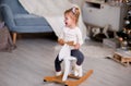Funny little girl preschooler with blond hair in a white sweater rides a rocking horse and smiles, grimaces and shows tongue
