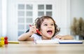 Funny little girl sit at desk at home doing homework, reading , writing and painting. Children paint. Kids draw. Royalty Free Stock Photo