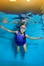 Funny little girl is swimming underwater in the pool on yellow light background in swimming glasses and purple dress. Royalty Free Stock Photo
