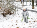 A funny little girl in a warm silver jumpsuit holds a toy shovel