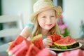 Funny little girl wearing straw hat biting a slice of watermelon outdoors on warm and sunny summer day. Royalty Free Stock Photo