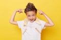 Funny little girl with wet hair wearing casual white T-shirt standing isolated over yellow background showing her hairbun with