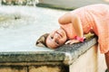 Funny little girl wetting hair in fountain hot summer day