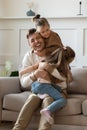 Funny little girls hugging smiling father sitting on couch