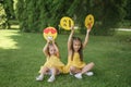 Funny little girls are sitting on lawn in the park with paper-cut emoji faces