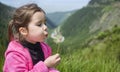 Funny little happy girl on the mountain top blowing on dandelion