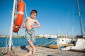 Funny little healthy boy in shorts stands on the pier with sea and blue sky background Royalty Free Stock Photo