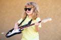 Funny little hipster musician child playing guitar. Portrait of a funny child with glasses practicing a song during a