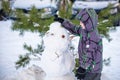 Funny little kid boy making a snowman and eating carrot, playing having fun with snow, outdoors on cold day. Active leisure childr