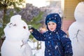 Funny little kid boy making a snowman and eating carrot, playing having fun with snow, outdoors on cold day. Active leisure chil Royalty Free Stock Photo