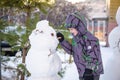 Funny little kid boy making a snowman and eating carrot, playing having fun with snow, outdoors on cold day. Active leisure childr