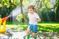 Funny little kid boy playing with a garden hose sprinkler on hot and sunny summer day. Child having fun with sprinkling Royalty Free Stock Photo