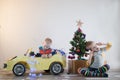 Funny little smiling kids driving toy car with Christmas tree. Happy child in colour fashion clothes bringing hewed xmas tree from Royalty Free Stock Photo