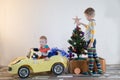 Funny little smiling kids driving toy car with Christmas tree. Happy child in colour fashion clothes bringing hewed xmas tree from Royalty Free Stock Photo