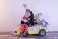 Funny little smiling kids driving toy car with Christmas tree. Happy child in colour fashion clothes bringing hewed xmas tree from Royalty Free Stock Photo