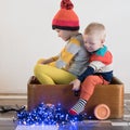 Funny little smiling kids driving toy car with Christmas tree. Happy child in colour fashion clothes bringing hewed xmas tree from Royalty Free Stock Photo