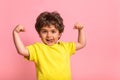 Funny little sportive kid boy in yellow shirt, showing his muscles. Happy strong nerd kindergarten child showing bicep