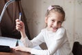 Funny little thin caucasian girl without some teeth holding pen in hand sitting at table during homework education