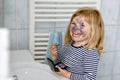 Funny little toddler girl using mother`s make up and painting face with eye shadows. Happy baby child making experiments Royalty Free Stock Photo