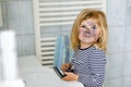 Funny little toddler girl using mother`s make up and painting face with eye shadows. Happy baby child making experiments Royalty Free Stock Photo