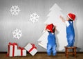 Funny Little twins dressed Santa hat, glue Christmas tree on wal Royalty Free Stock Photo