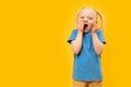 Funny little white-haired girl with two ponytails in blue T-shirt. Yellow background. Child laughs by covering his mouth with her Royalty Free Stock Photo