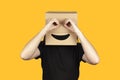 Funny man with a box on his head makes binoculars from his hands, isolated on a yellow background Royalty Free Stock Photo