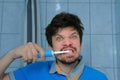 Funny man is brushing teeth usin electric toothbrush and making cheerful faces. Royalty Free Stock Photo