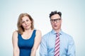 A funny man in glasses and a tie looks askance at the bust of a young woman in a tight dress, who is nearby, on a light blue Royalty Free Stock Photo