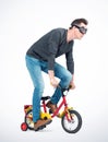 Funny man in goggles, jeans and black t-shirt pedals a children`s bicycle Royalty Free Stock Photo