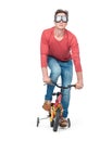 Funny man in goggles, jeans and a red t-shirt pedals a children`s bicycle, isolated on white background. Royalty Free Stock Photo