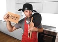 Funny man holding pan with pot on head in apron at kitchen asking for help Royalty Free Stock Photo