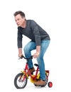 Funny man in jeans and black t-shirt pedals a children`s bicycle, isolated on white background. Royalty Free Stock Photo