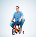 Funny man in jeans and t-shirt on a children`s bike, on light background. Royalty Free Stock Photo