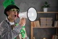 Funny man in leprechaun hat with megaphone in hand announcing the start of big St.Patricks day sales and discounts