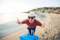 Funny man with suitcase showing thumbs up against the blue ocean. Travel concept. Royalty Free Stock Photo