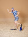 Funny man in vintage style striped swimsuit, diving mask, snorkel and flippers walking on sand Royalty Free Stock Photo