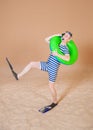 Funny man in vintage style striped swimsuit, inflatable ring, diving mask, snorkel and flippers walking on sand Royalty Free Stock Photo