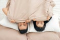 Funny married couple lying in bed and hiding under white blanket, looking at camera with eyes full of joy Royalty Free Stock Photo