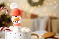 Funny marshmallow snowman in cup of hot drink against blurred festive lights, closeup. Space for text Royalty Free Stock Photo