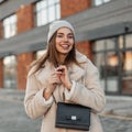 Funny model of a young woman in fashionable youth spring clothes with a leather handbag is standing in a parking lot near a