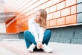 Funny modern young woman in stylish sneakers in vintage jeans in an elegant sweater is sitting on the pavement